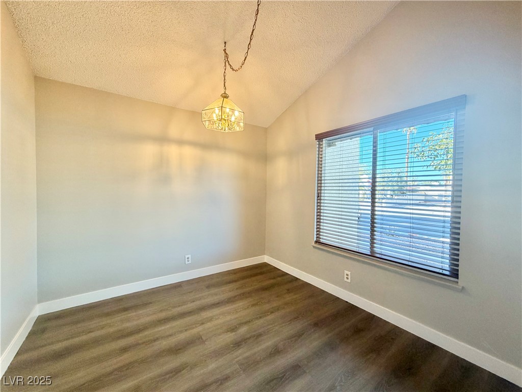 6401 Waterthrush Way Las Vegas, NV 89103 - Photo 3 of 19 Spare room featuring vaulted ceiling, dark wood finished floors, a textured ceiling, and a chandelier