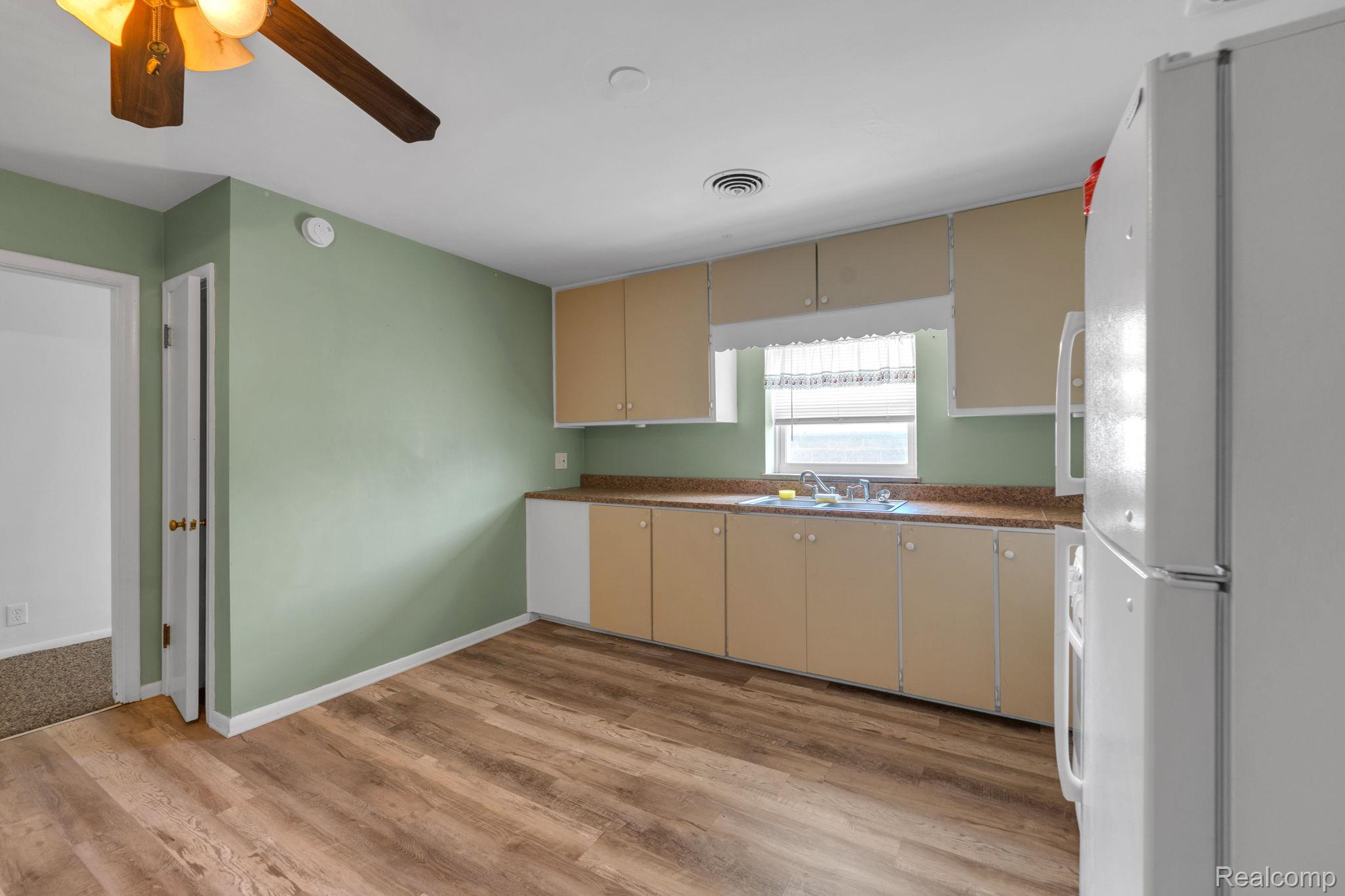 5223 Allen Road Allen Park, MI 48101 - Photo 8 of 12 Kitchen featuring wood-finish flooring, light green wall paint, overhead cabinetry with light-colored doors, a window above the sink, and a white refrigerator