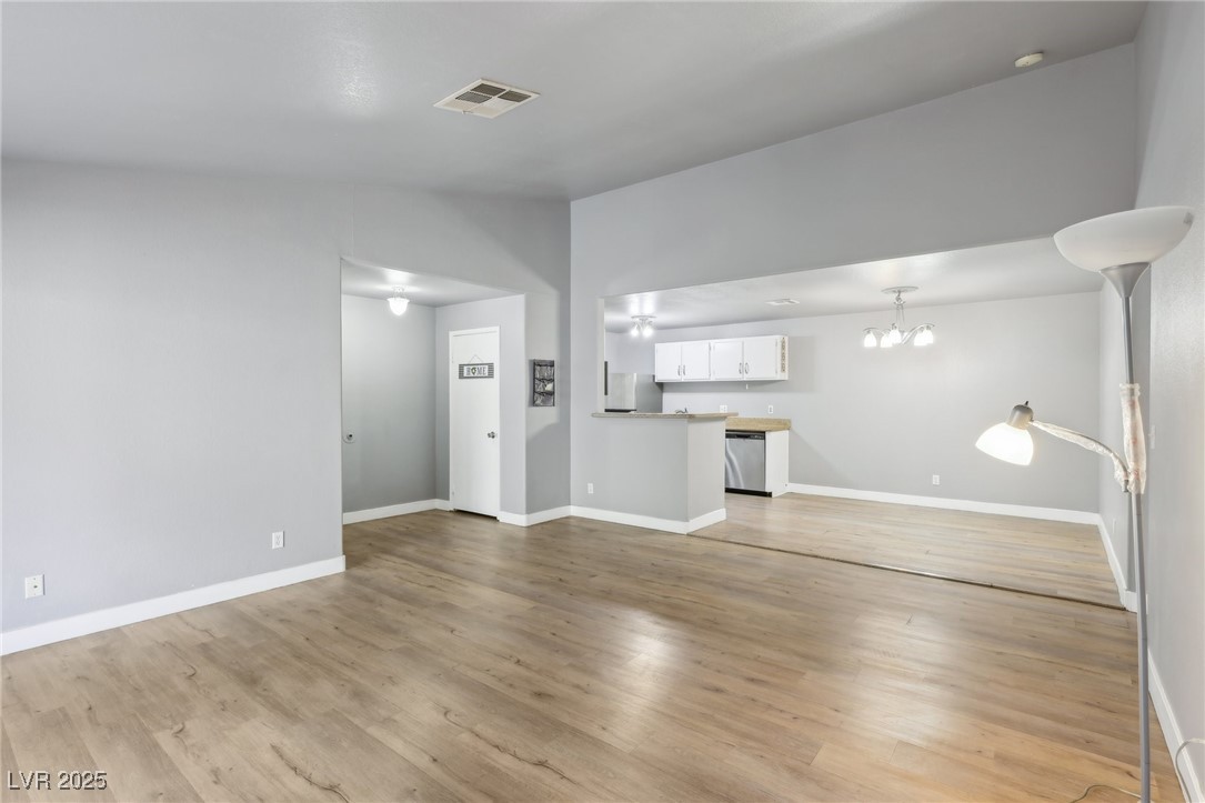 5241 South Lindell Road, Unit 202 Las Vegas, NV 89118 - Photo 7 of 35 Unfurnished living room featuring lofted ceiling, light wood-style flooring, a notable chandelier, visible vents, and baseboards