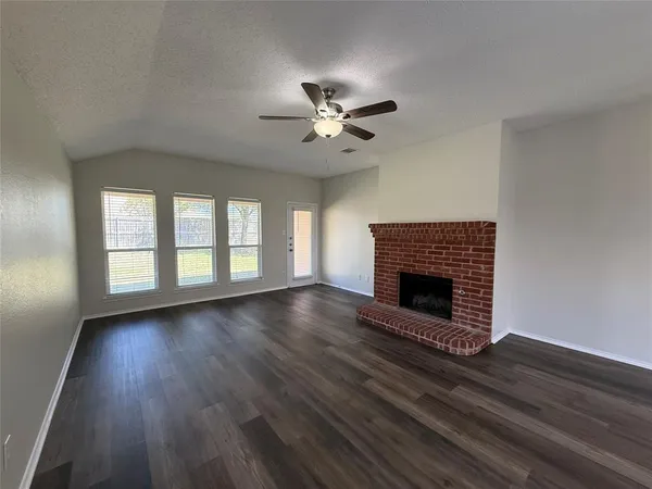 an empty room with wooden floor a ceiling fan a fireplace and windows