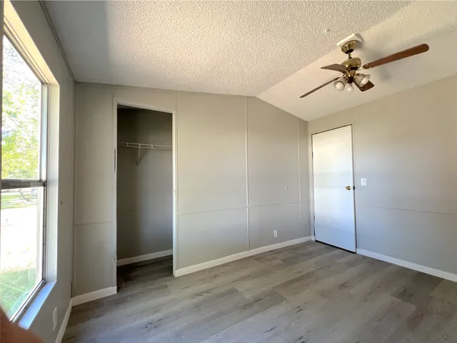 an empty room with wooden floor fan and windows