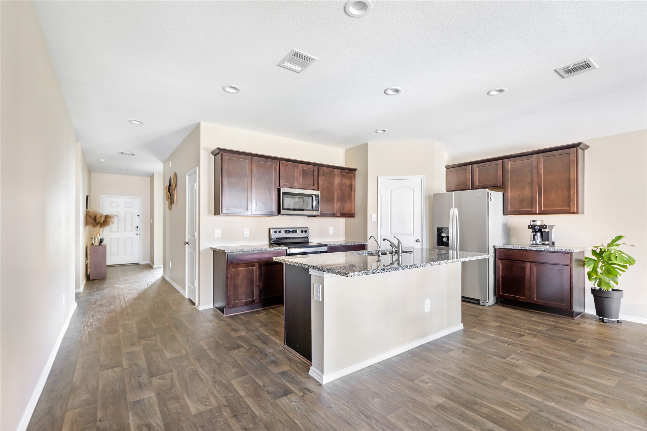 811 Republic Road New Caney, TX 77357 - Photo 23 of 37 This modern kitchen features dark wood cabinets, stainless steel appliances, and a large island with granite countertops. The open layout connects to a spacious hallway with wood like flooring and ample natural light.