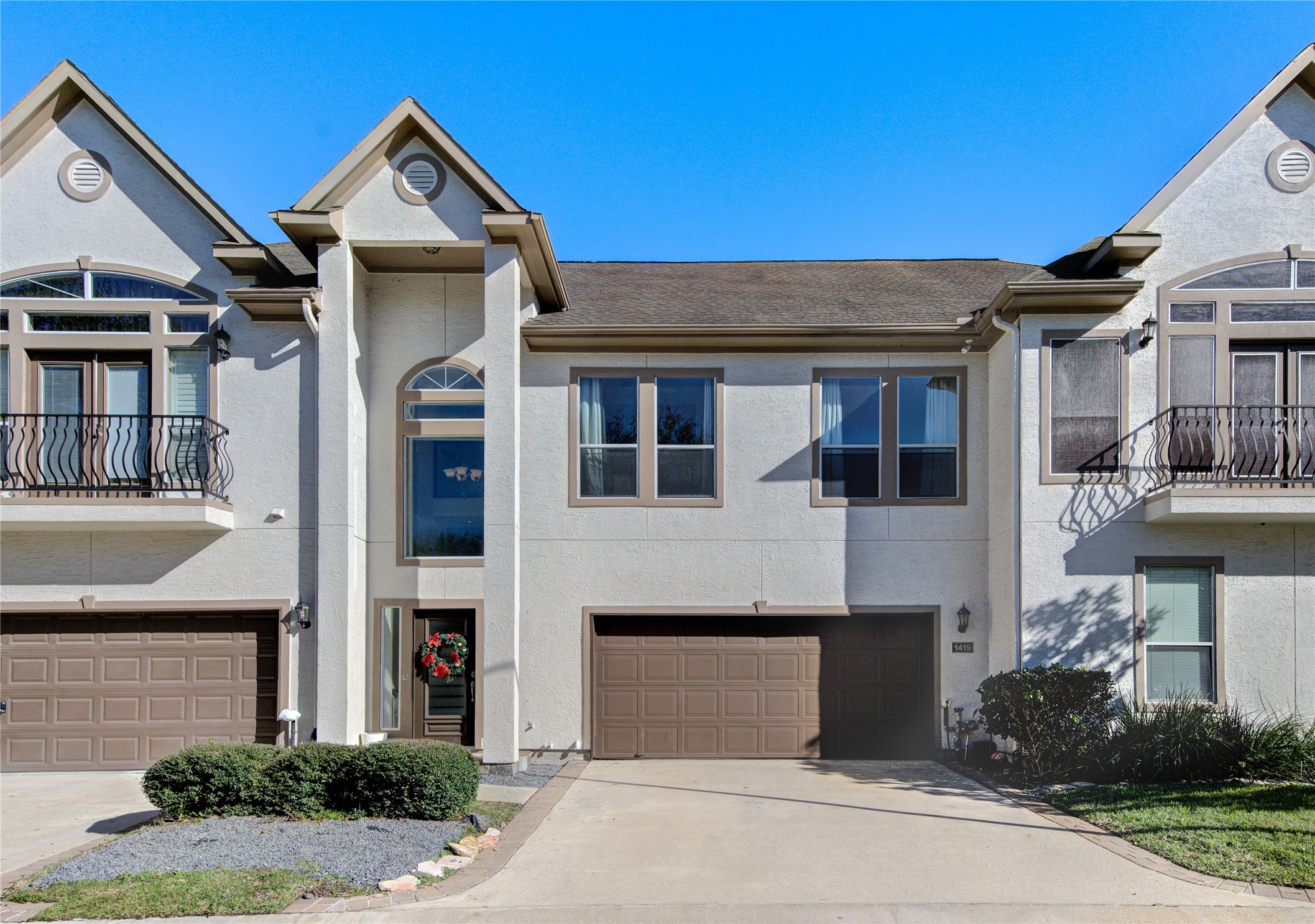 This photo showcases a modern townhouse with a symmetrical design, featuring two levels, a double garage, and decorative windows. The facade is accented by neutral tones and a well-maintained front yard.