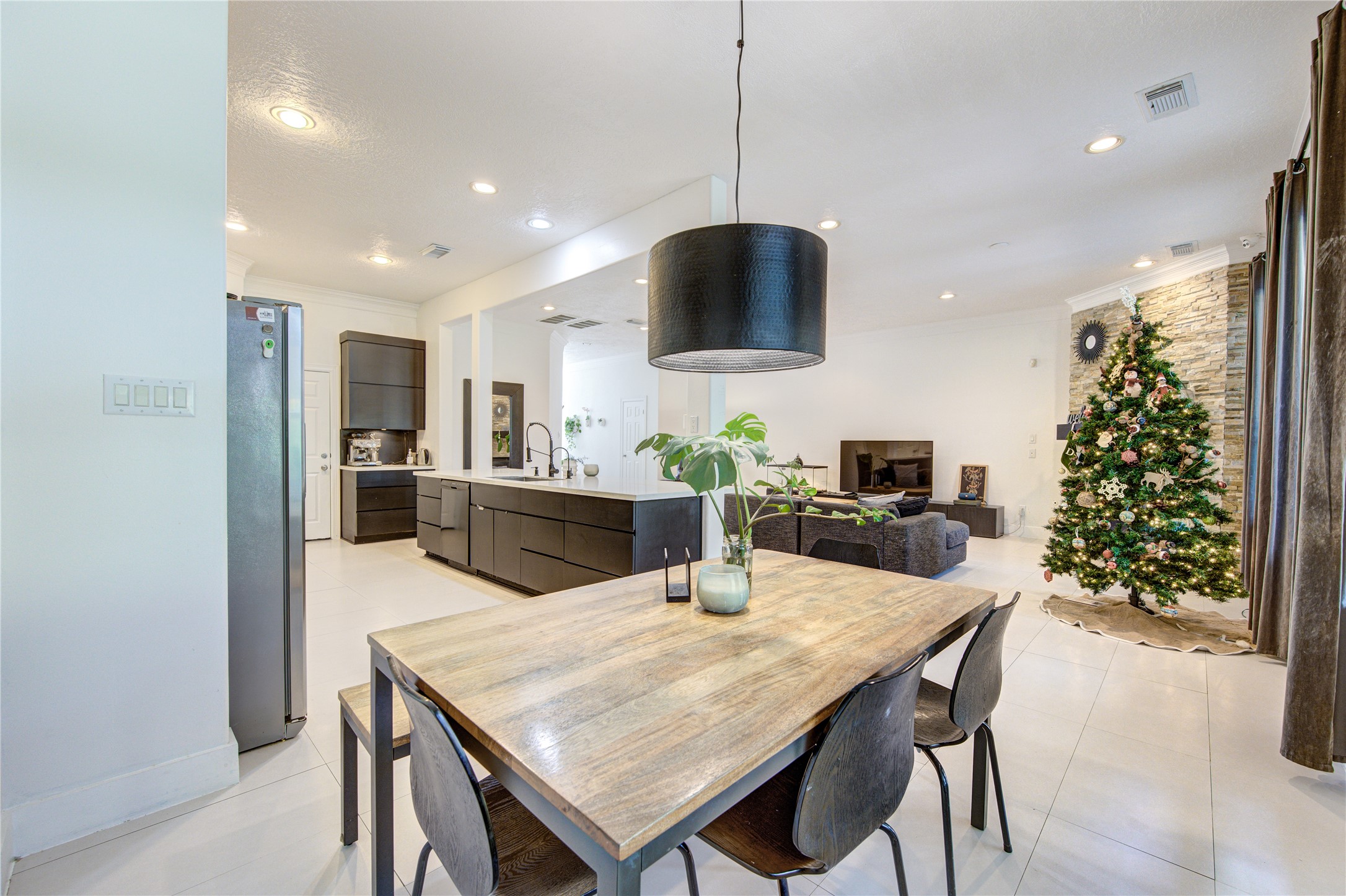 1419 Baldwin Square Lane Houston, TX 77077 - Photo 14 of 45 This open-concept living space features a modern kitchen with sleek cabinetry and a spacious dining area. The room is bright with recessed lighting, and a cozy living area includes a stone accent wall and a holiday tree, creating a warm, inviting atmosphere.