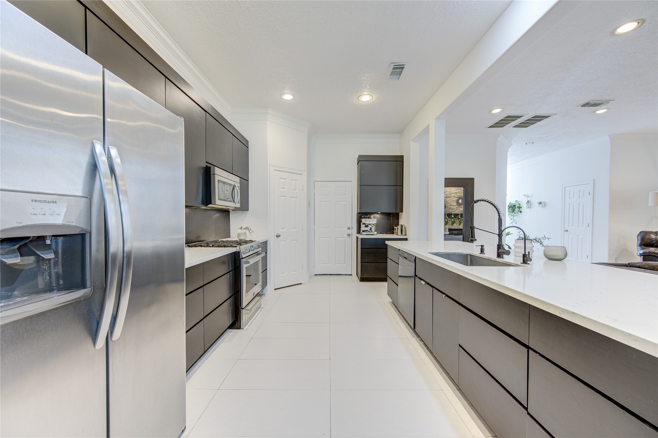 1419 Baldwin Square Lane Houston, TX 77077 - Photo 17 of 45 This modern kitchen features sleek dark cabinets, stainless steel appliances, and a spacious white countertop with dual sinks. It's well-lit with recessed lighting and offers an open layout that connects to the living area, providing a contemporary and functional space.