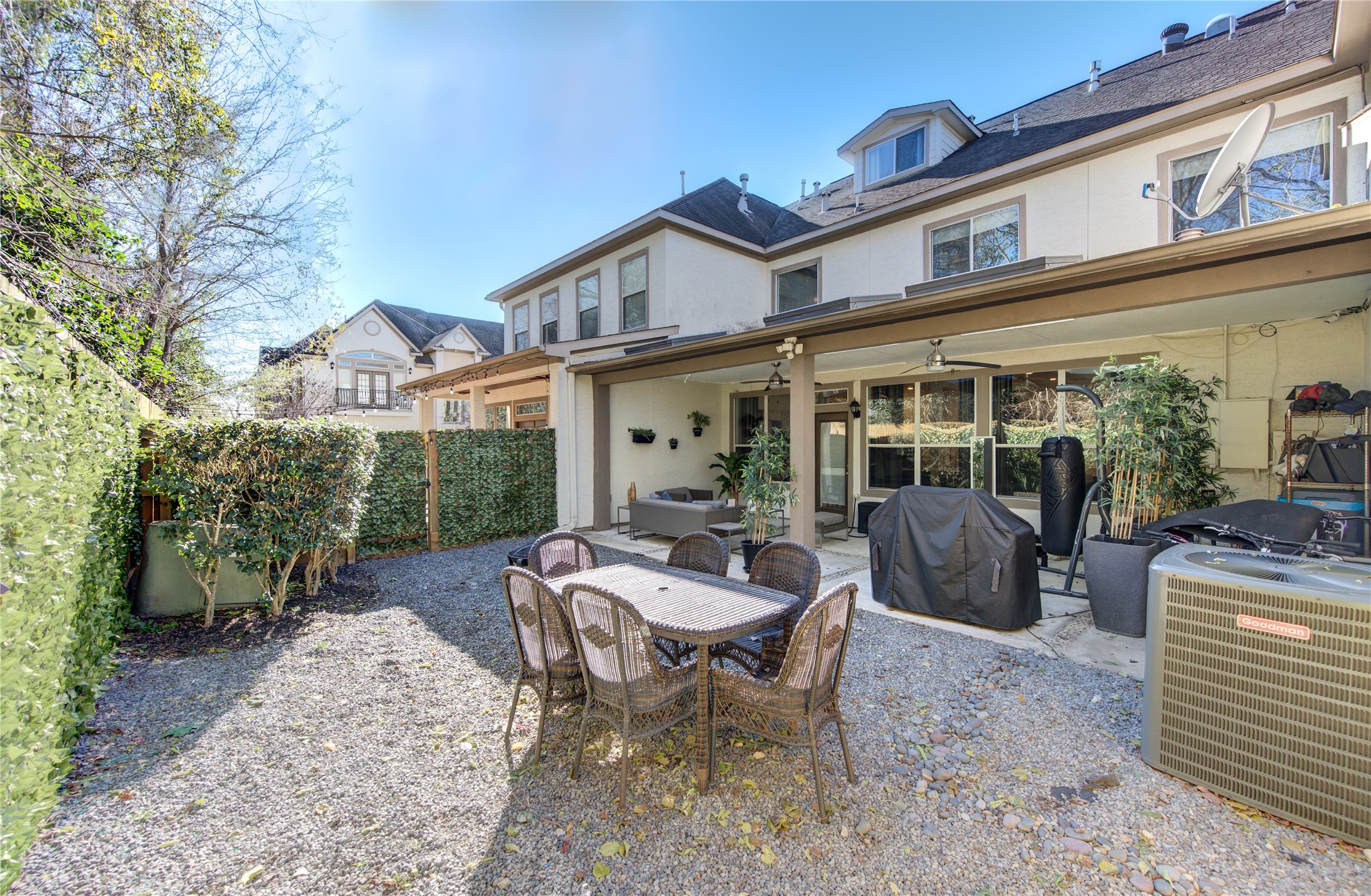 1419 Baldwin Square Lane Houston, TX 77077 - Photo 2 of 45 This photo showcases a charming, private backyard area of a townhouse with a gravel surface. It includes a covered patio with outdoor seating and dining area, surrounded by lush greenery and privacy hedges. The space is ideal for outdoor gatherings and relaxation.