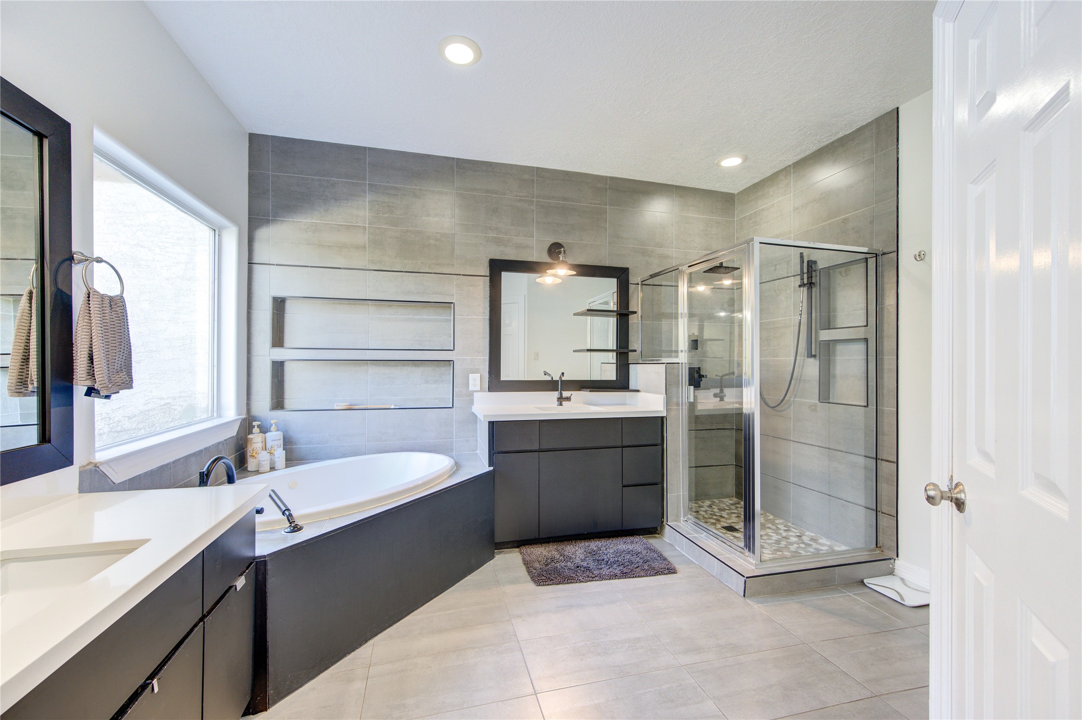 1419 Baldwin Square Lane Houston, TX 77077 - Photo 25 of 45 This modern bathroom features a large soaking tub, a glass-enclosed shower, and a sleek vanity with ample storage. The neutral tile design and large window provide a bright and spacious feel.