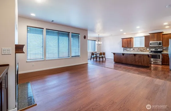 a living room with stainless steel appliances furniture wooden floor and a kitchen view