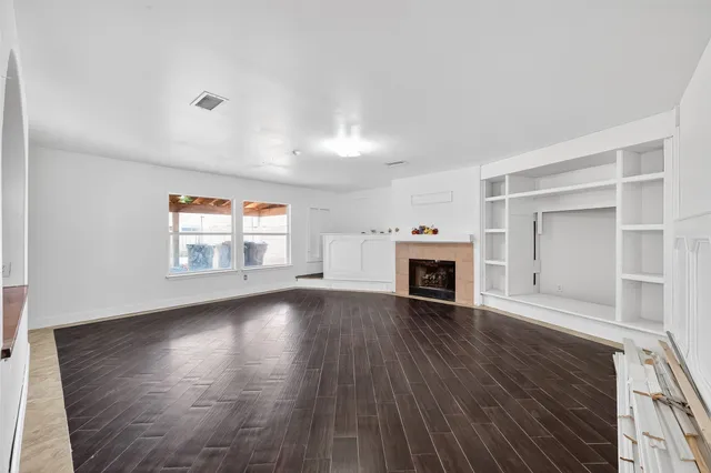 an empty room with wooden floor fireplace and windows