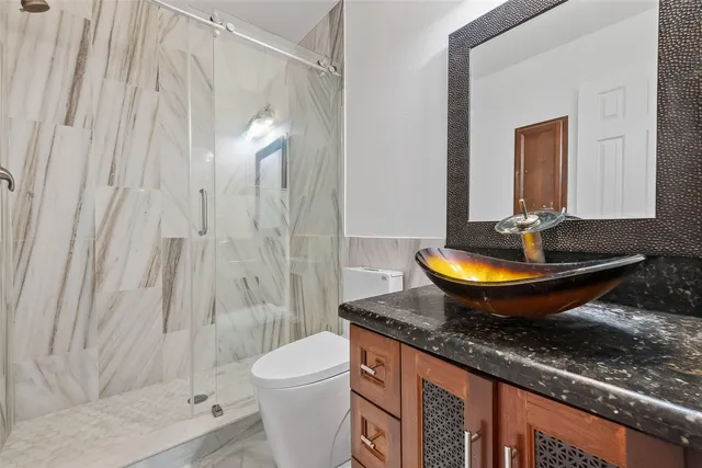 a bathroom with a granite countertop sink a toilet a mirror and shower