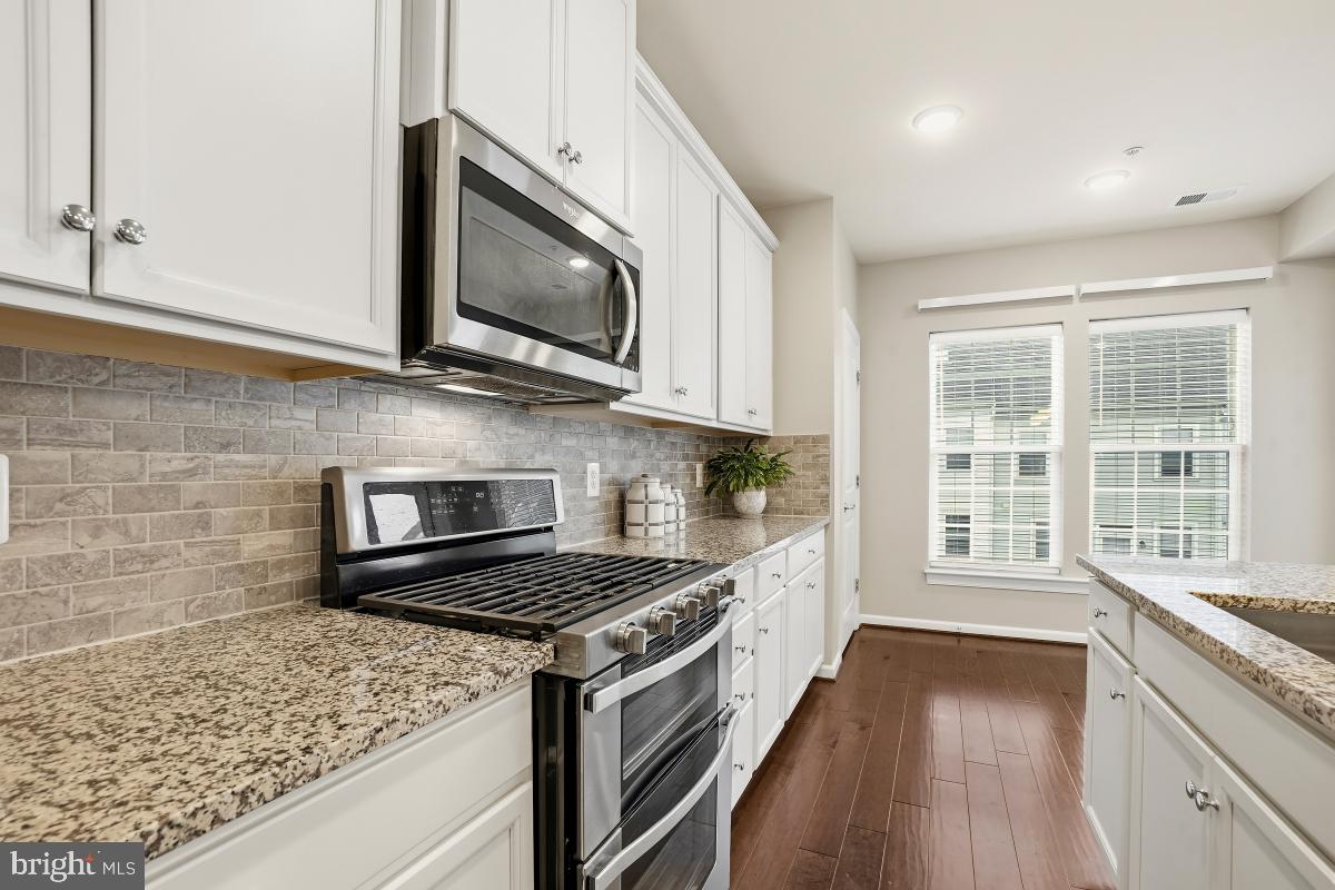 23517 Public House Road, Unit H Clarksburg, MD 20871 - Photo 23 of 49 a kitchen with stainless steel appliances kitchen island granite countertop a stove a sink and a microwave