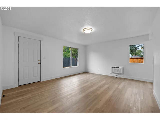 a view of an empty room with window and wooden floor