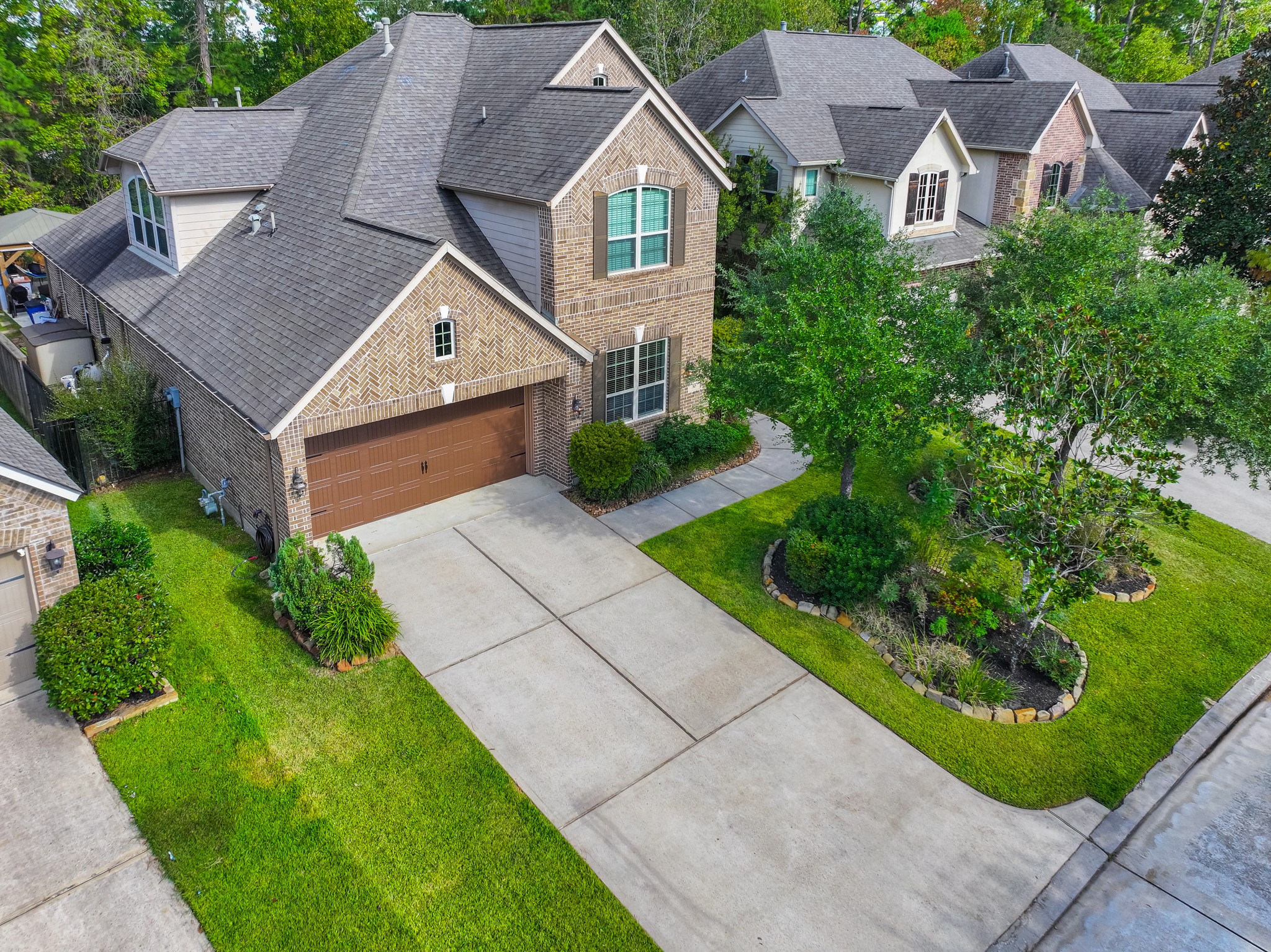 30 Fury Ranch Place The Woodlands, TX 77375 - Photo 2 of 47 This photo shows a charming two-story brick home with a well-maintained front lawn and a spacious driveway leading to a two-car garage. The house is surrounded by lush greenery and trees, providing a serene and inviting atmosphere.