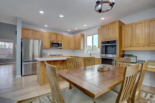 a dining hall with stainless steel appliances granite countertop a stove a sink dishwasher a dining table and chairs with wooden floor