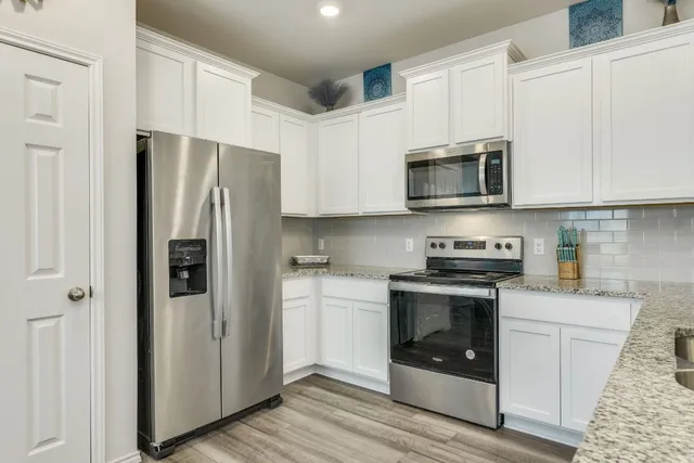 a kitchen with stainless steel appliances granite countertop white cabinets a refrigerator a stove a microwave oven with white cabinets