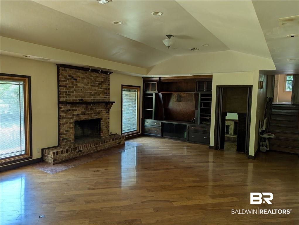 3608 Linden Lane Mobile, AL 36608 - Photo 19 of 20 Unfurnished living room featuring a fireplace, brick wall, vaulted ceiling, and hardwood / wood-style floors