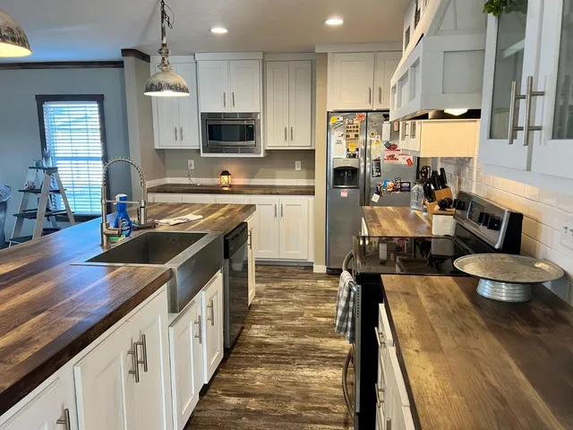 a kitchen with stainless steel appliances a stove a sink dishwasher a refrigerator white cabinets and wooden floor