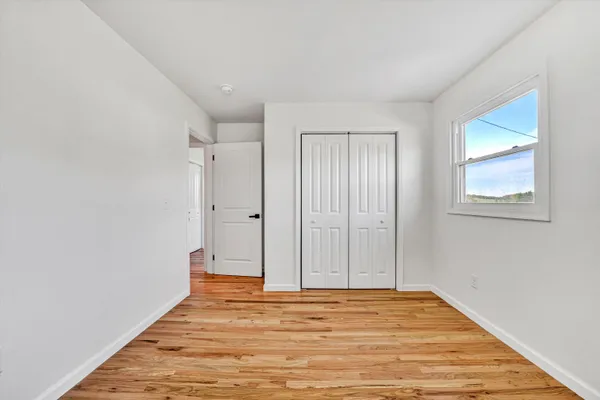 a view of an empty room with wooden floor and a window