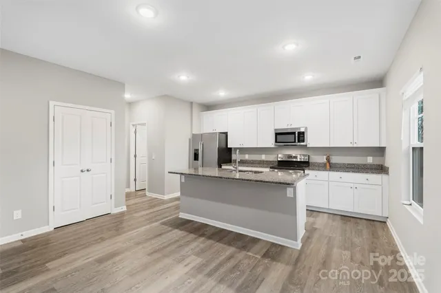 a kitchen with stainless steel appliances granite countertop a stove top oven a sink dishwasher and a refrigerator with wooden floor