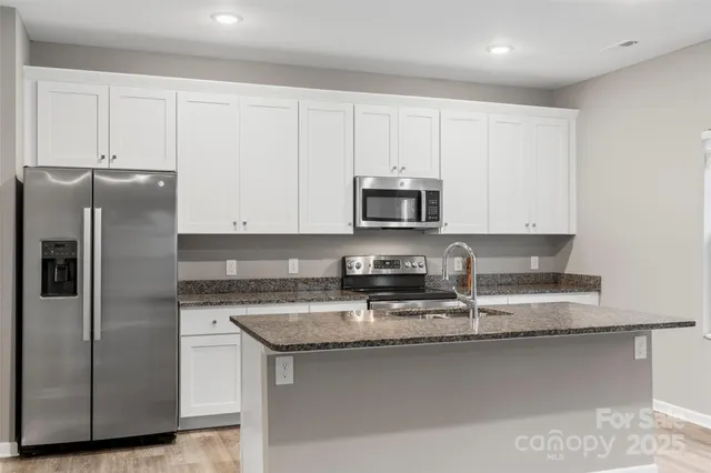 a kitchen with stainless steel appliances granite countertop a refrigerator a stove a sink and white cabinets