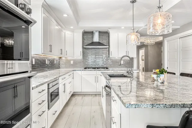 a open kitchen with stainless steel appliances granite countertop a stove a sink dishwasher and white cabinets with wooden floor