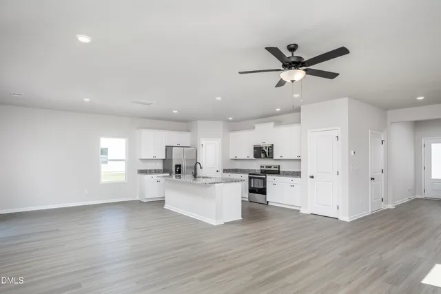 a kitchen with stainless steel appliances granite countertop a stove top oven a sink a refrigerator and white cabinets with wooden floor