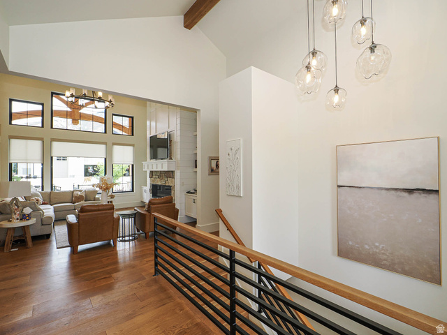 3167 South Mapleton Ests Drive Mapleton, UT 84664 - Photo 5 of 30 Vaulted ceiling with exposed wood beam, wood-finish flooring, staircase with wood handrail and black metal balusters, stacked stone fireplace with built-in shiplap cabinetry, and multiple large windows