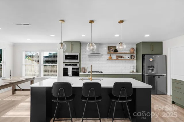 a kitchen with stainless steel appliances granite countertop a stove a sink a refrigerator a dining table and chairs with wooden floor