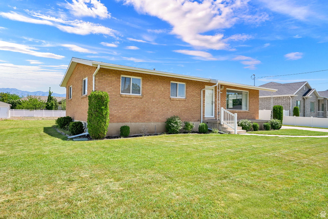 2467 South 2000 West Syracuse, UT 84075 - Photo 2 of 28 Brick exterior residence featuring a front lawn with established landscaping, a white entry door with an awning, and a front porch with white railing