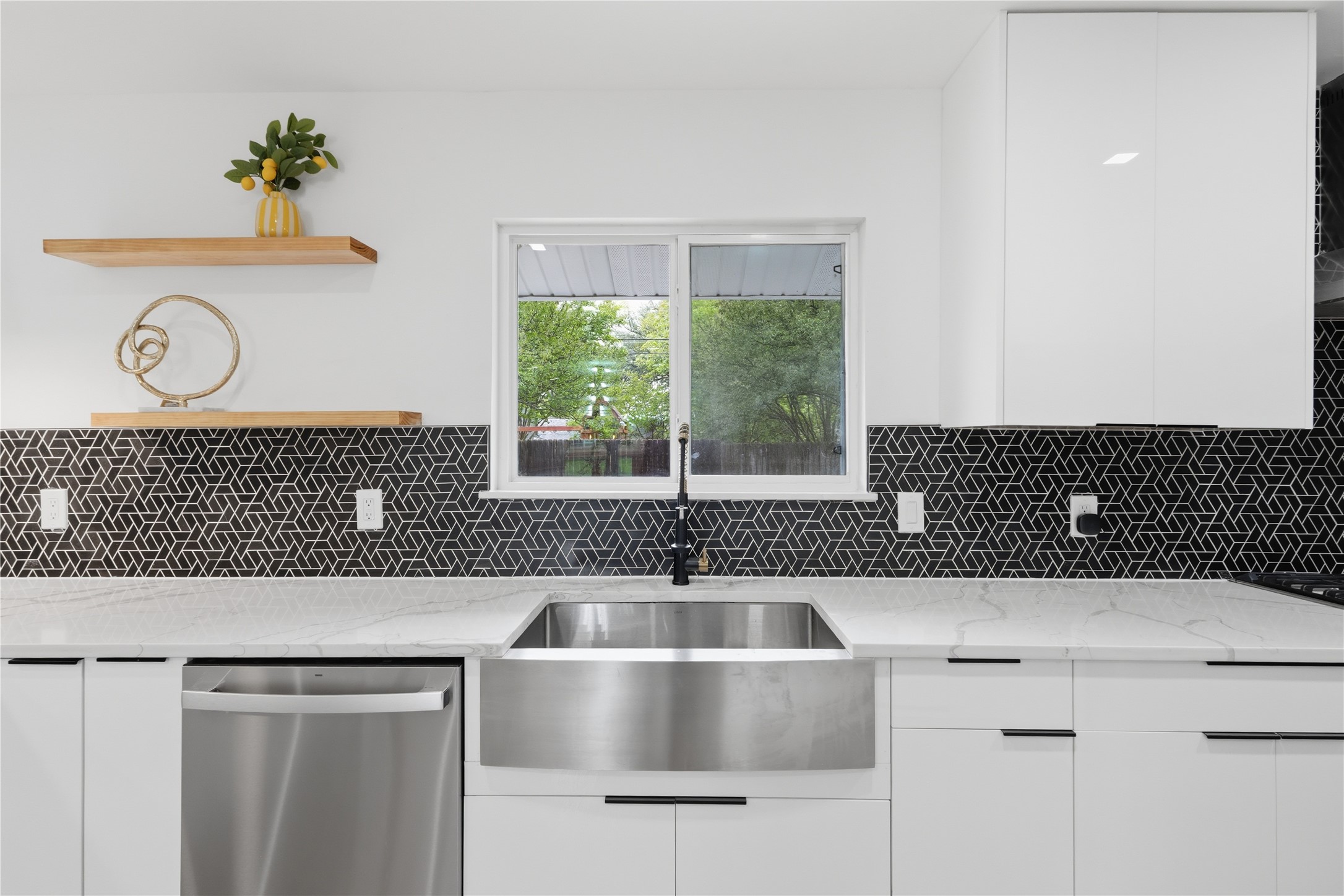 5604 Coventry Lane Austin, TX 78723 - Photo 13 of 33 Modern kitchen featuring a farmhouse sink, stainless steel dishwasher, white flat-panel cabinetry, geometric pattern tile backsplash, and light-toned countertops