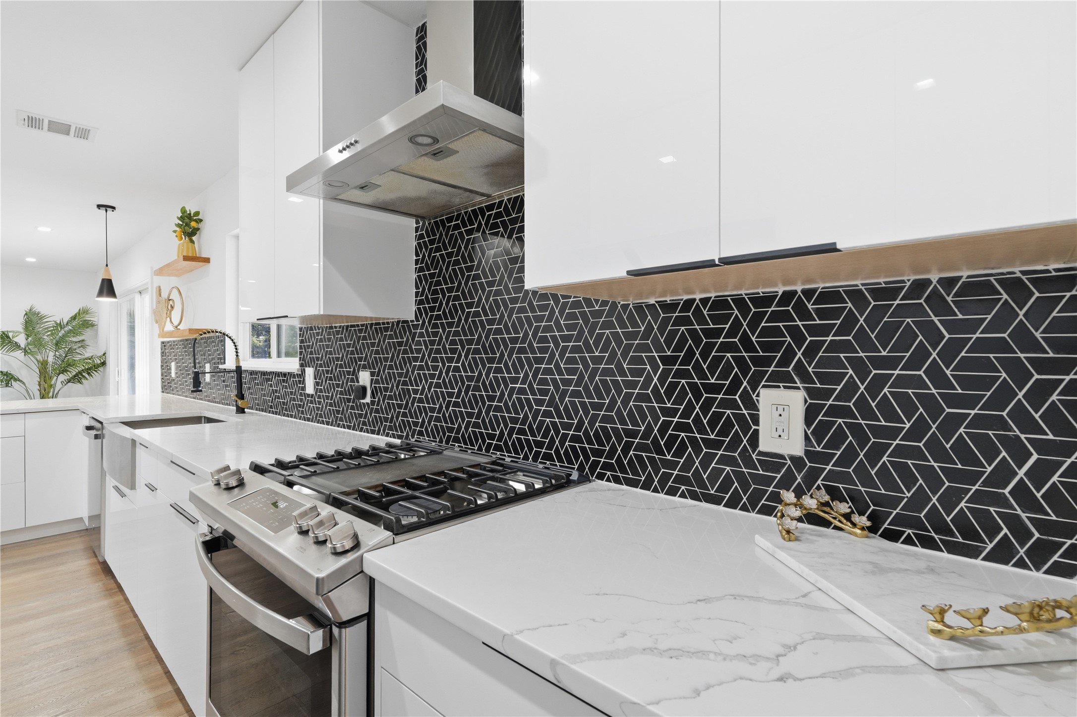 5604 Coventry Lane Austin, TX 78723 - Photo 15 of 33 Contemporary kitchen featuring white cabinetry, a geometric black tile backsplash, stainless steel gas range with coordinating hood, and light-toned countertops