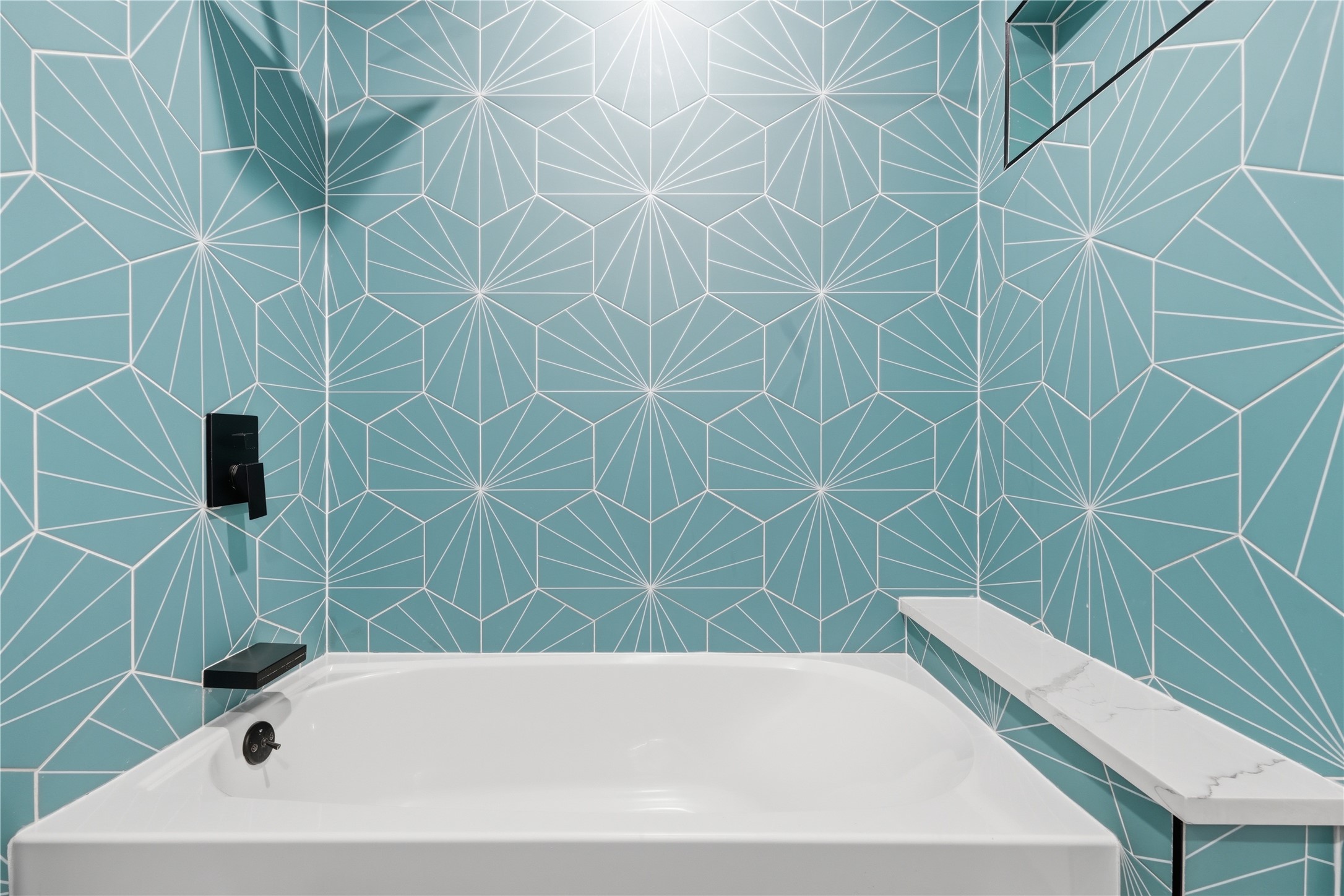 5604 Coventry Lane Austin, TX 78723 - Photo 17 of 33 Bathtub featuring matte black fixtures, a built-in shelf with a stone-finish surface, and geometric patterned wall tiling in a teal hue
