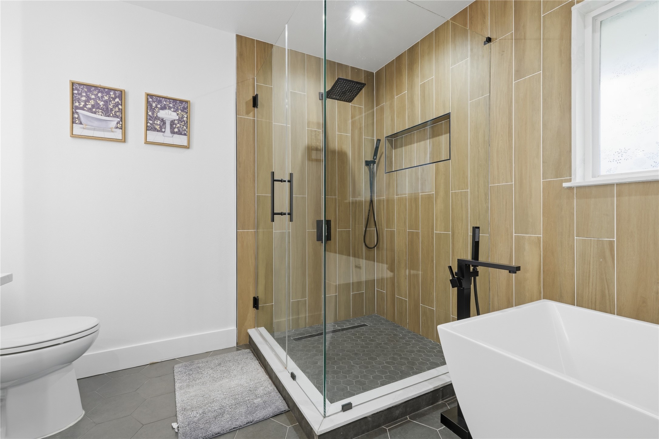 5604 Coventry Lane Austin, TX 78723 - Photo 24 of 33 Modern bathroom featuring a freestanding soaking tub with a matte black floor-mounted faucet, a glass-enclosed shower with wood-finish tile surround and rainfall showerhead, and hexagon floor tiles