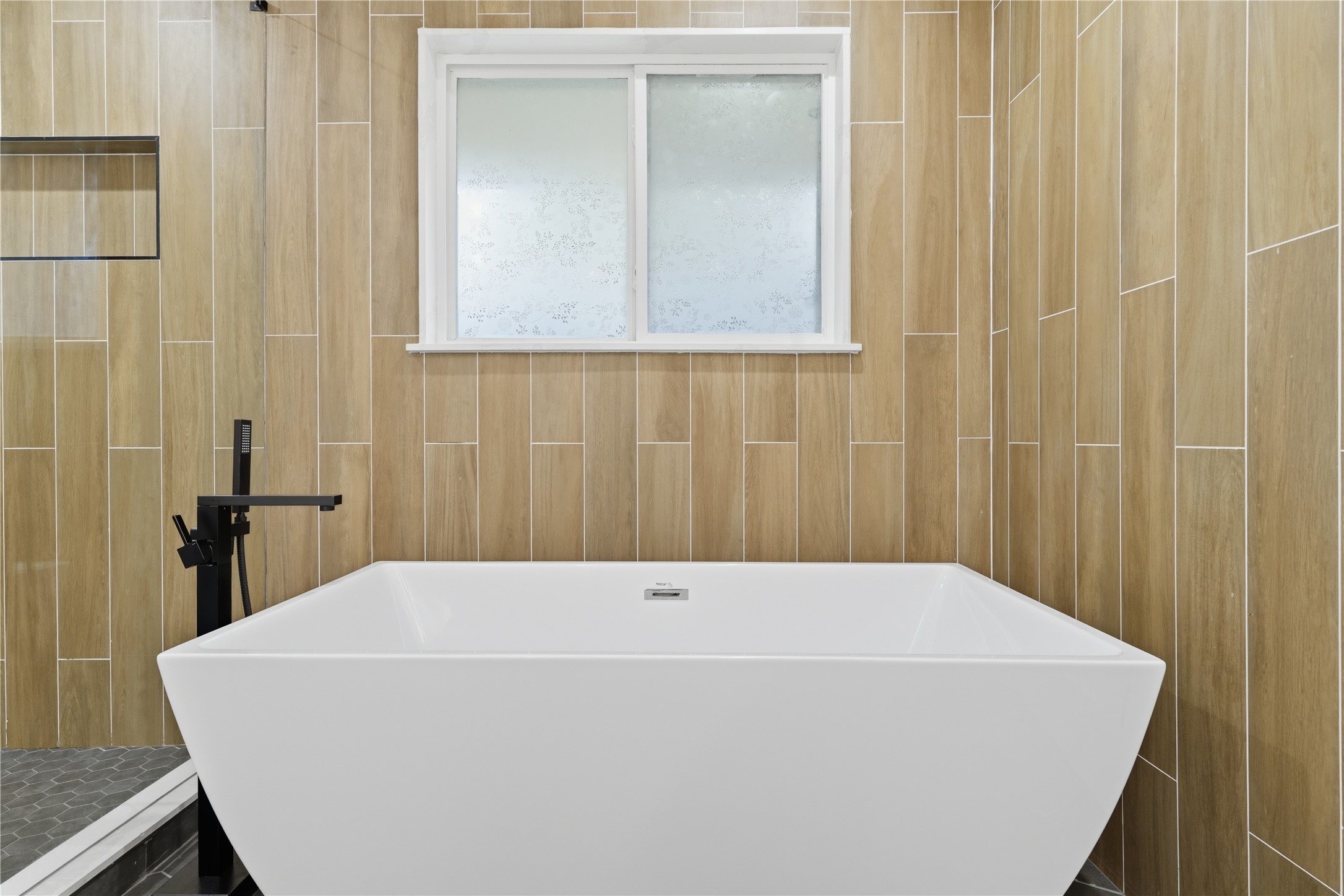 5604 Coventry Lane Austin, TX 78723 - Photo 25 of 33 Freestanding soaking tub with a matte black floor-mounted faucet, set against wood-finish vertical tile