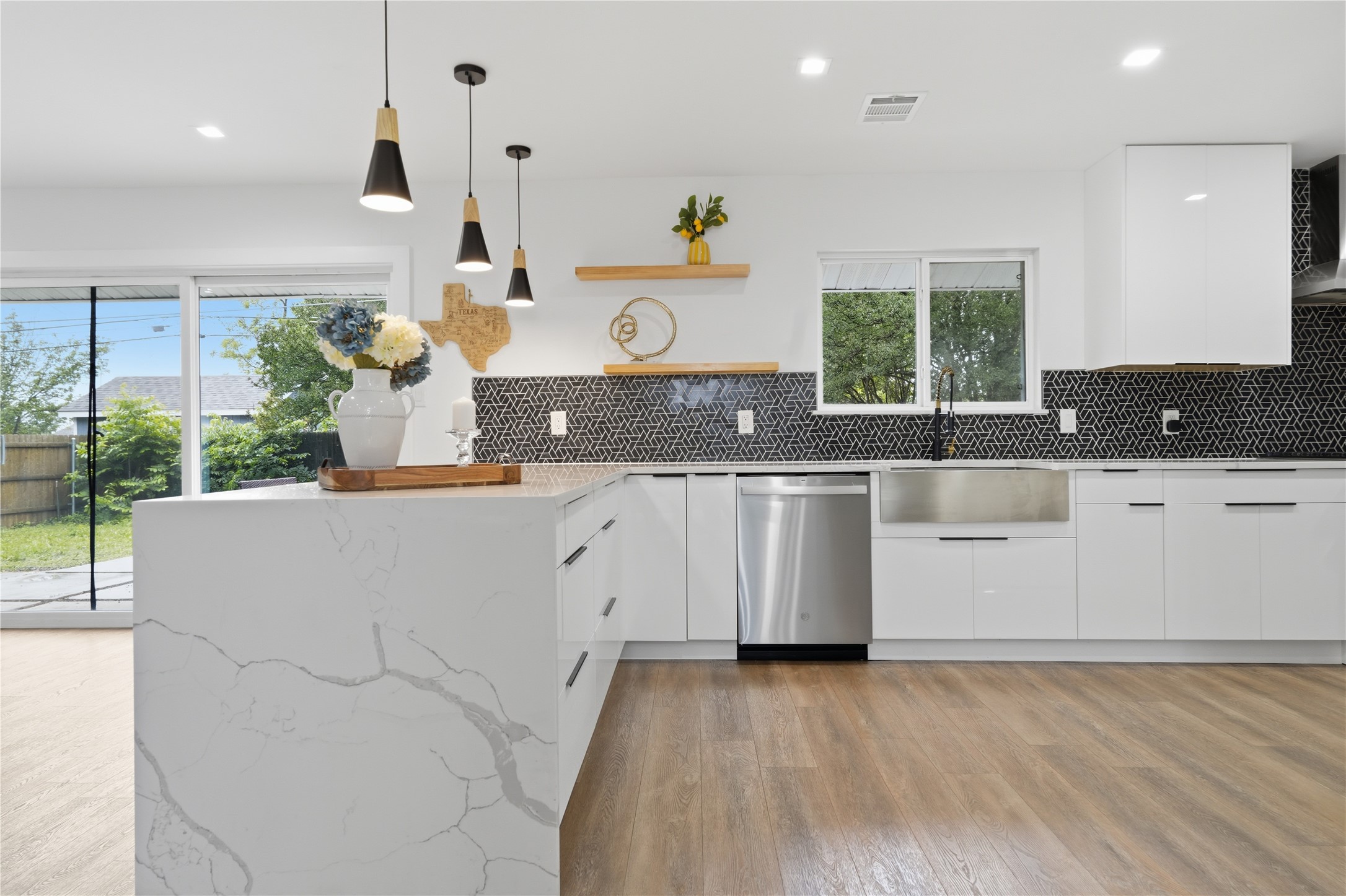 5604 Coventry Lane Austin, TX 78723 - Photo 9 of 33 Contemporary kitchen featuring a waterfall island with a quartz countertop, wood-finish flooring, and a patterned black backsplash