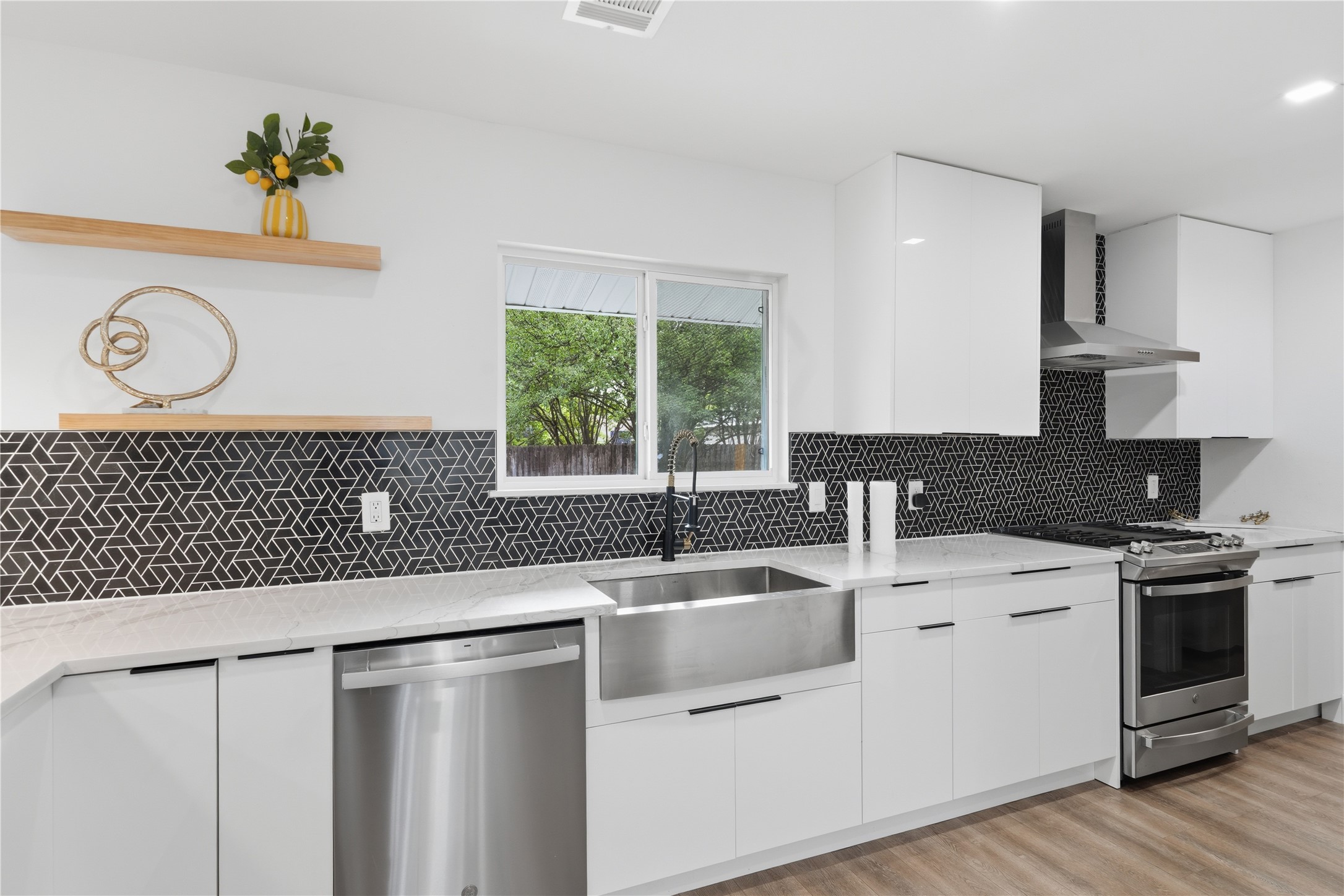 5604 Coventry Lane Austin, TX 78723 - Photo 10 of 33 Contemporary kitchen featuring white cabinetry, a geometric black and white tile backsplash, light-toned countertops, and stainless steel appliances