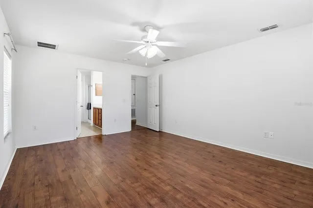 a view of an empty room with wooden floor and a ceiling fan