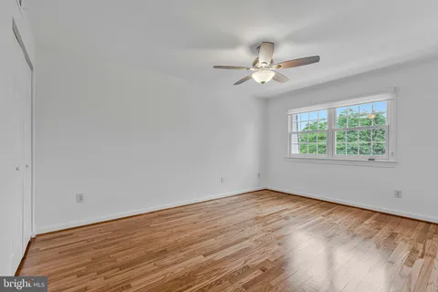 an empty room with wooden floor ceiling fan and windows