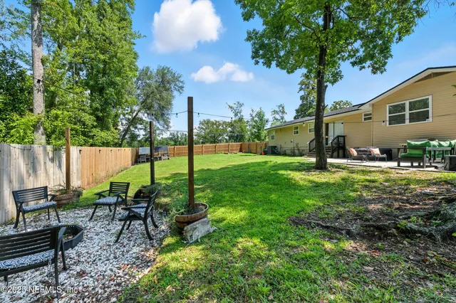 a view of a backyard with table and chairs potted plants and large tree