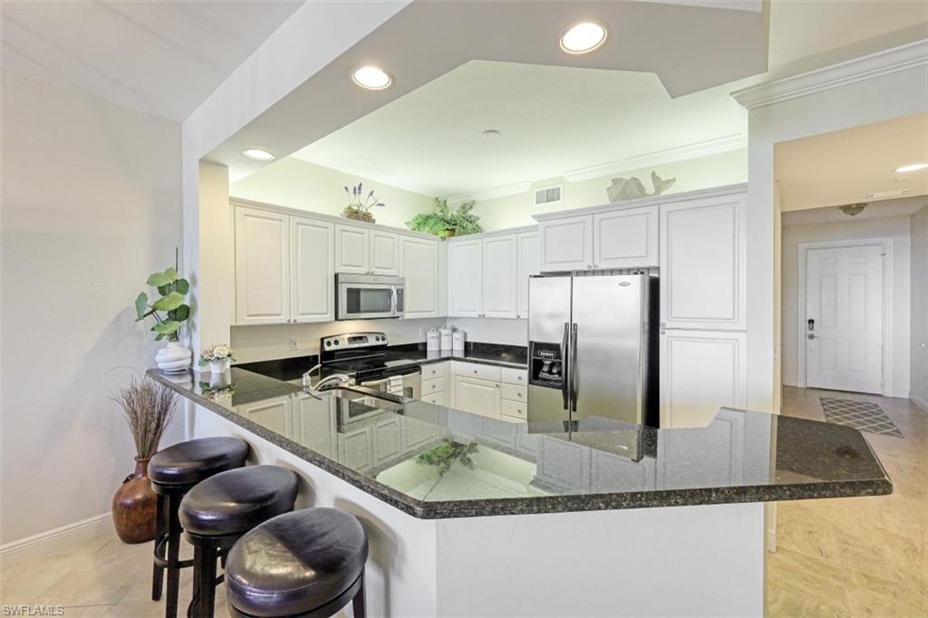 400 Flagship Drive, Unit 504 Naples, FL 34108 - Photo 6 of 38 Kitchen with recessed lighting, dark stone counters, appliances with stainless steel finishes, a breakfast bar area, and a peninsula