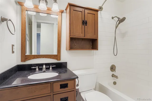 a bathroom with a granite countertop sink vanity mirror bathtub shower and a toilet