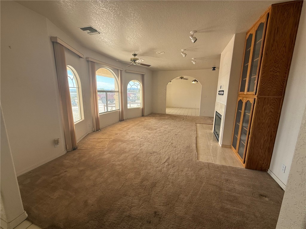 1845 Dunlap Road Fort Mohave, AZ 86426 - Photo 3 of 16 Unfurnished living room with light colored carpet, a textured ceiling, arched walkways, a fireplace, and a ceiling fan