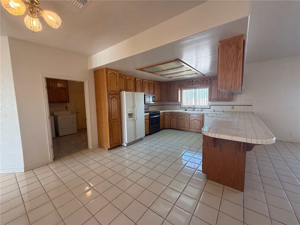 1845 Dunlap Road Fort Mohave, AZ 86426 - Photo 4 of 16 Kitchen featuring tile countertops, brown cabinetry, a peninsula, a breakfast bar, and white appliances