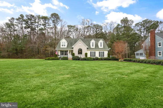 a view of a white house in front of a big yard with large trees