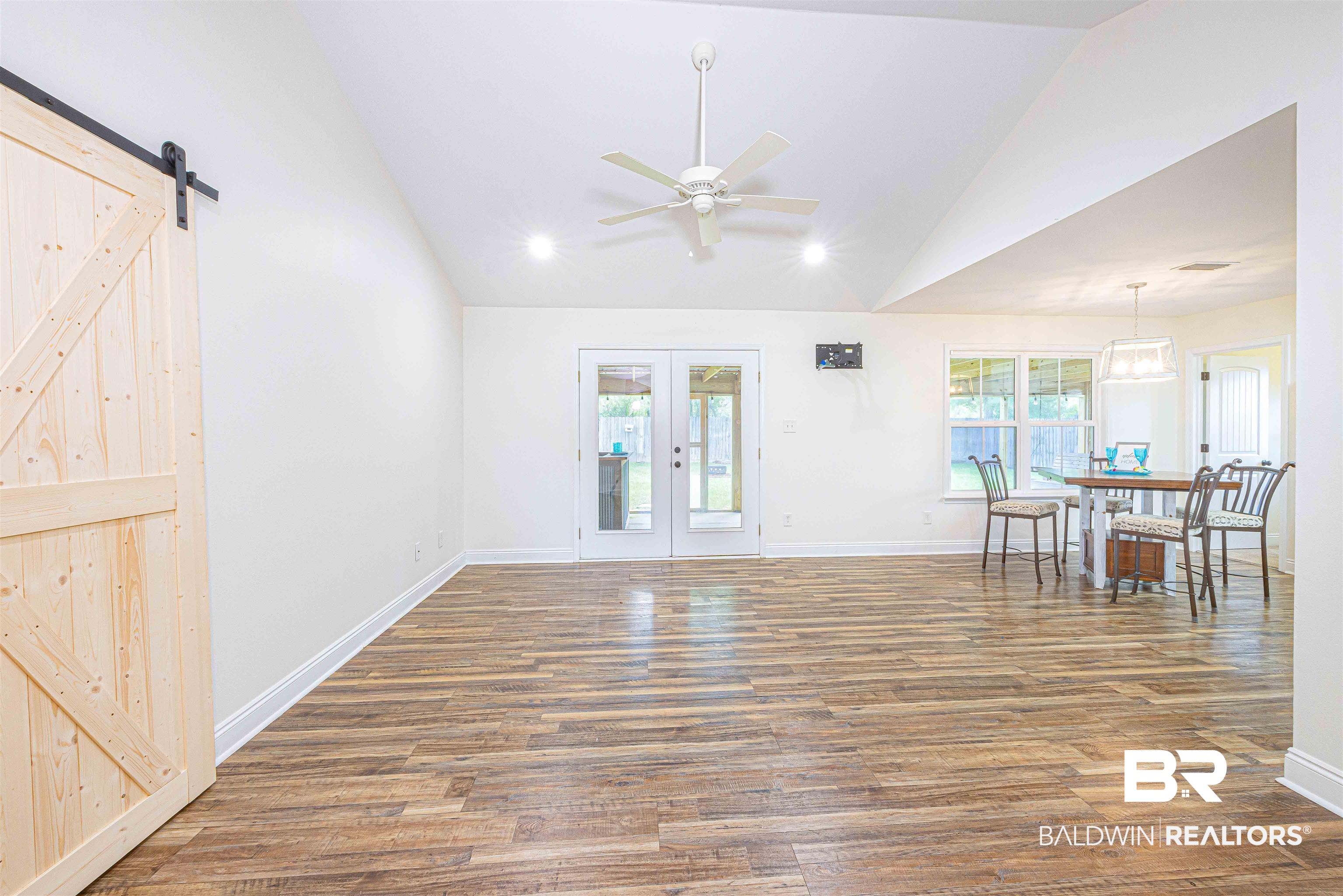 18675 Explorer Drive Loxley, AL 36551 - Photo 7 of 42 Unfurnished living room featuring vaulted ceiling, ceiling fan, wood finished floors, a barn door, and french doors