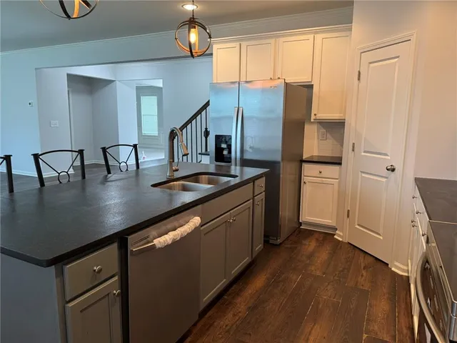 a kitchen with stainless steel appliances granite countertop a refrigerator a sink a stove and white cabinets with wooden floor