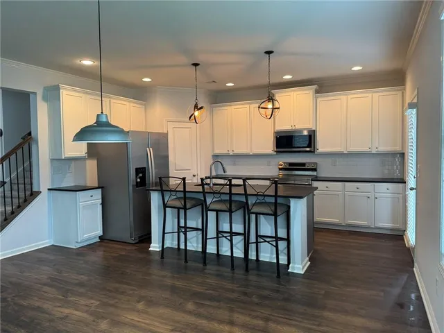 a kitchen with stainless steel appliances granite countertop a stove a sink a refrigerator and white cabinets with wooden floor