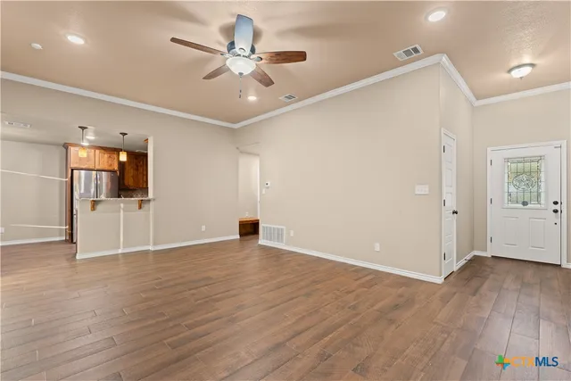 a view of an empty room with wooden floor and a ceiling fan