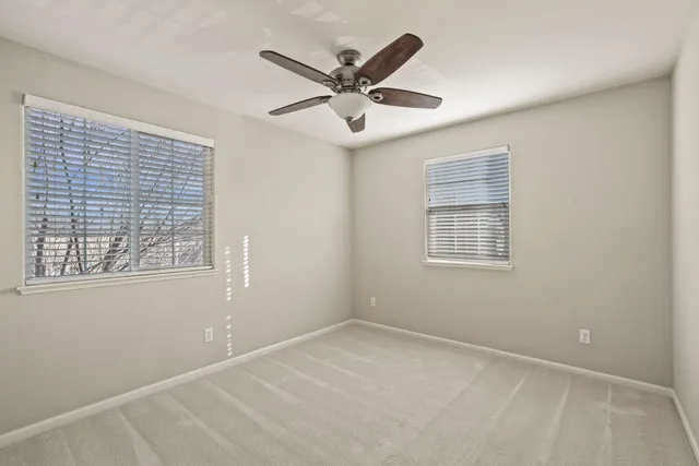 an empty room with ceiling fan and windows