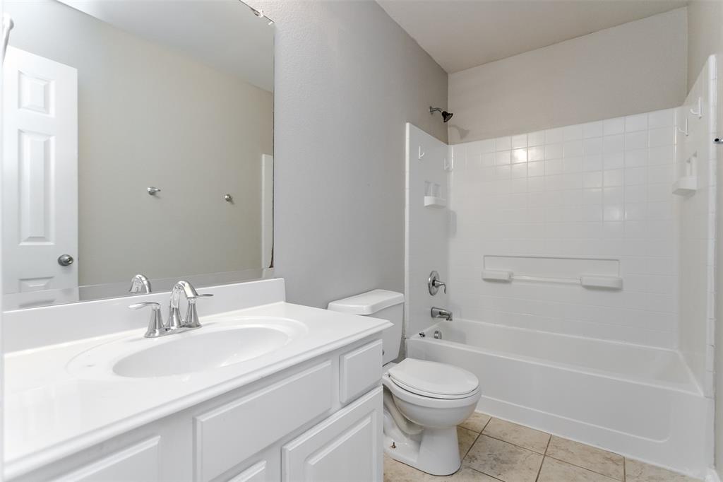 203 Arabian Road Waxahachie, TX 75165 - Photo 20 of 24 Bathroom featuring a white vanity with an integrated sink, a rectangular mirror, a toilet, a white bathtub with tile surround, and light-toned floor tile
